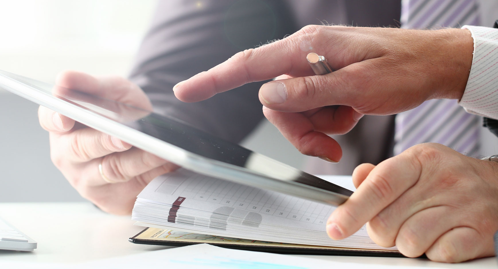 Zwei Personen besprechen Unterlagen, eine Hand zeigt auf den Bildschirm eines Tablets