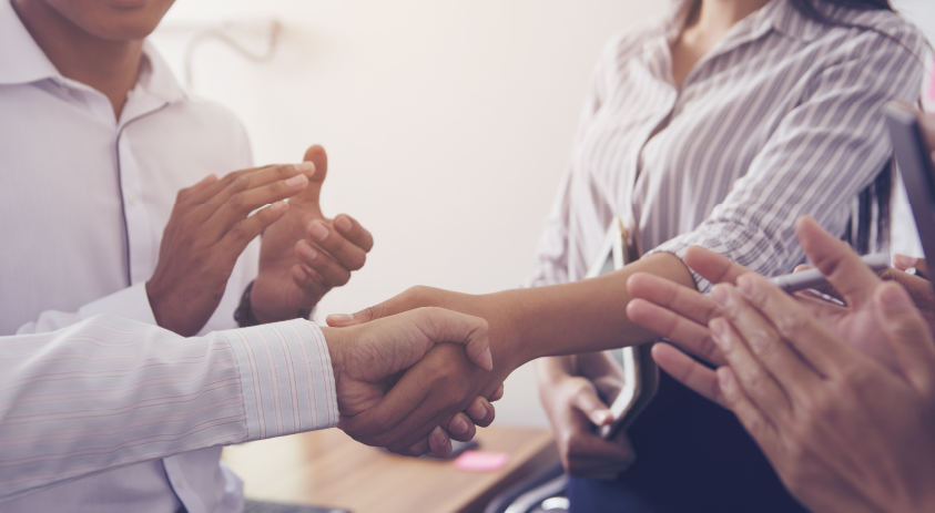 Zwei Personen geben sich die Hand, andere klatschen Beifall