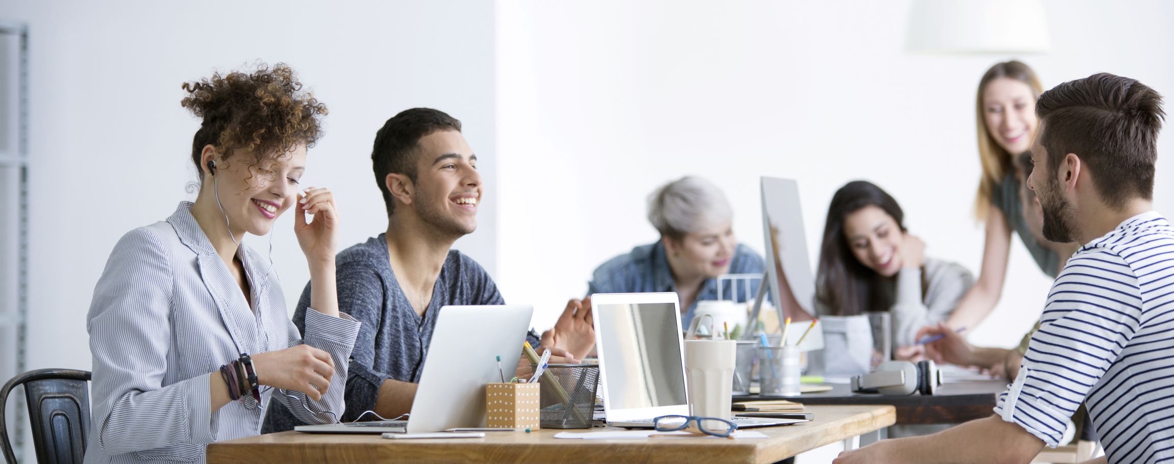 Fünf Personen lachen gemeinsam an einem Besprechungstisch mit Laptops